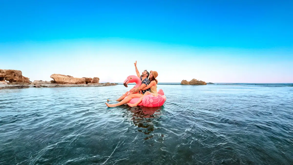 IOC Clinica dental — Dos personas en un flotador de flamenco rosa sobre un lago.