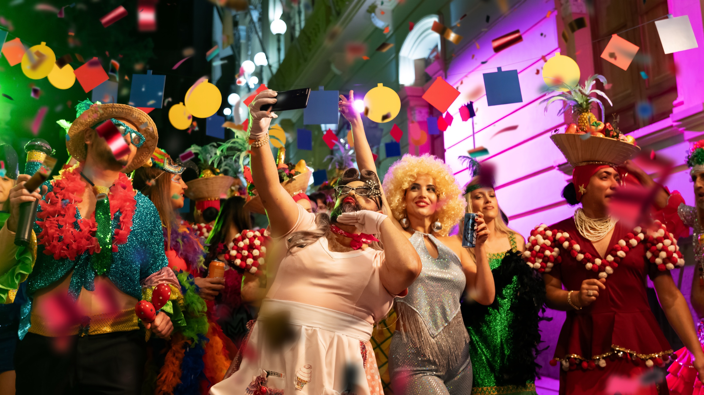 Lidl | Lo que nos une en Carnaval — Lidl — Crowd of dancers in colourful Carnaval costumes with feathered hats taking phone selfies surrounded by confetti and stage lights in the streets of the Canary Islands.
