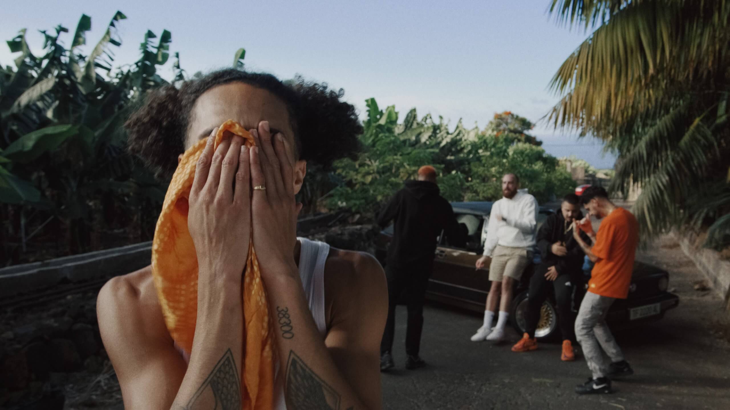 No le Bajes — A man with a towel over his face is standing in front of a group of people.