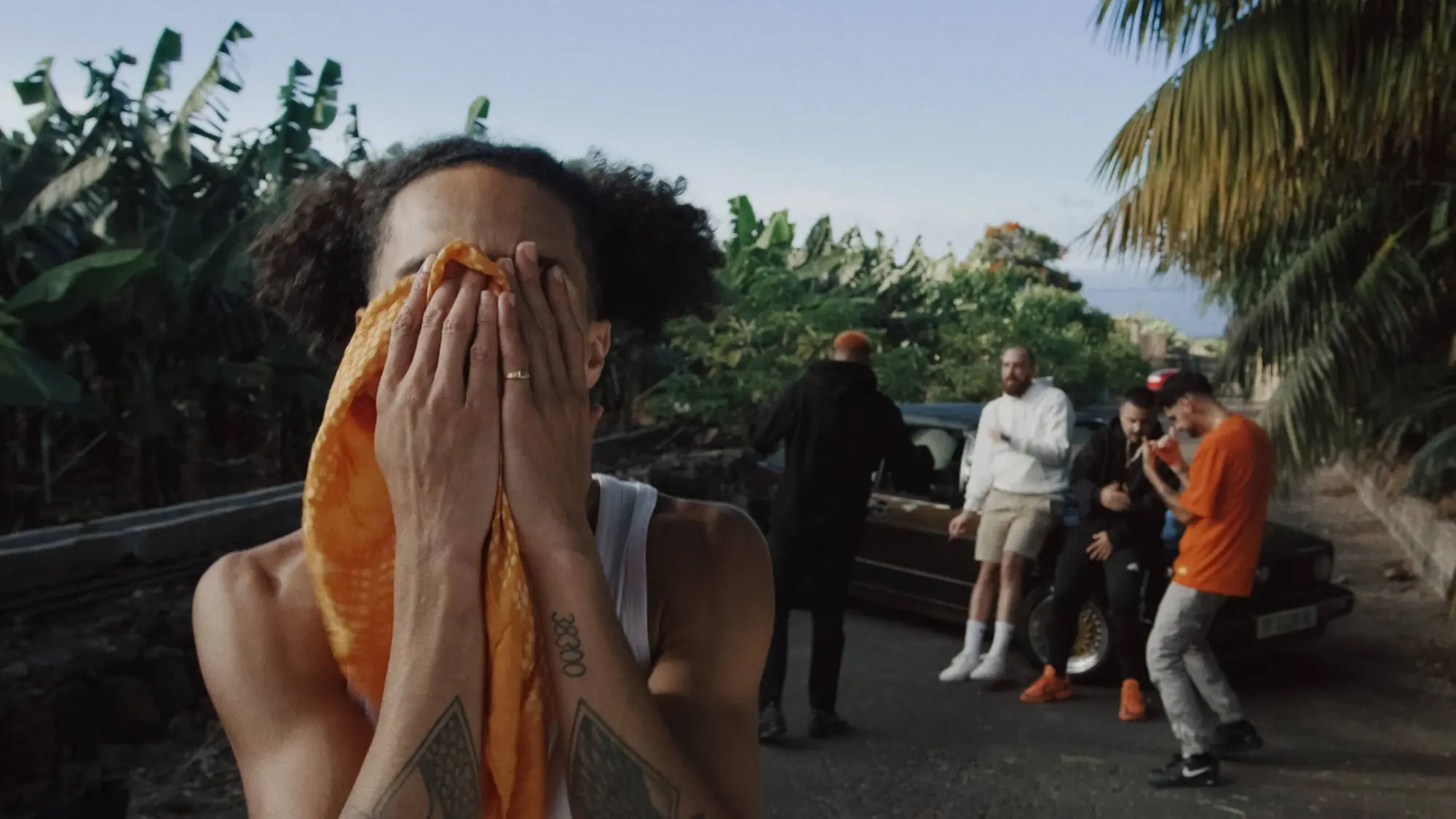 No le Bajes — A man with a towel over his face is standing in front of a group of people.